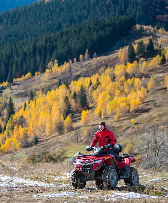 Bărbat pe un ATV roșu, pe un traseu montan toamna